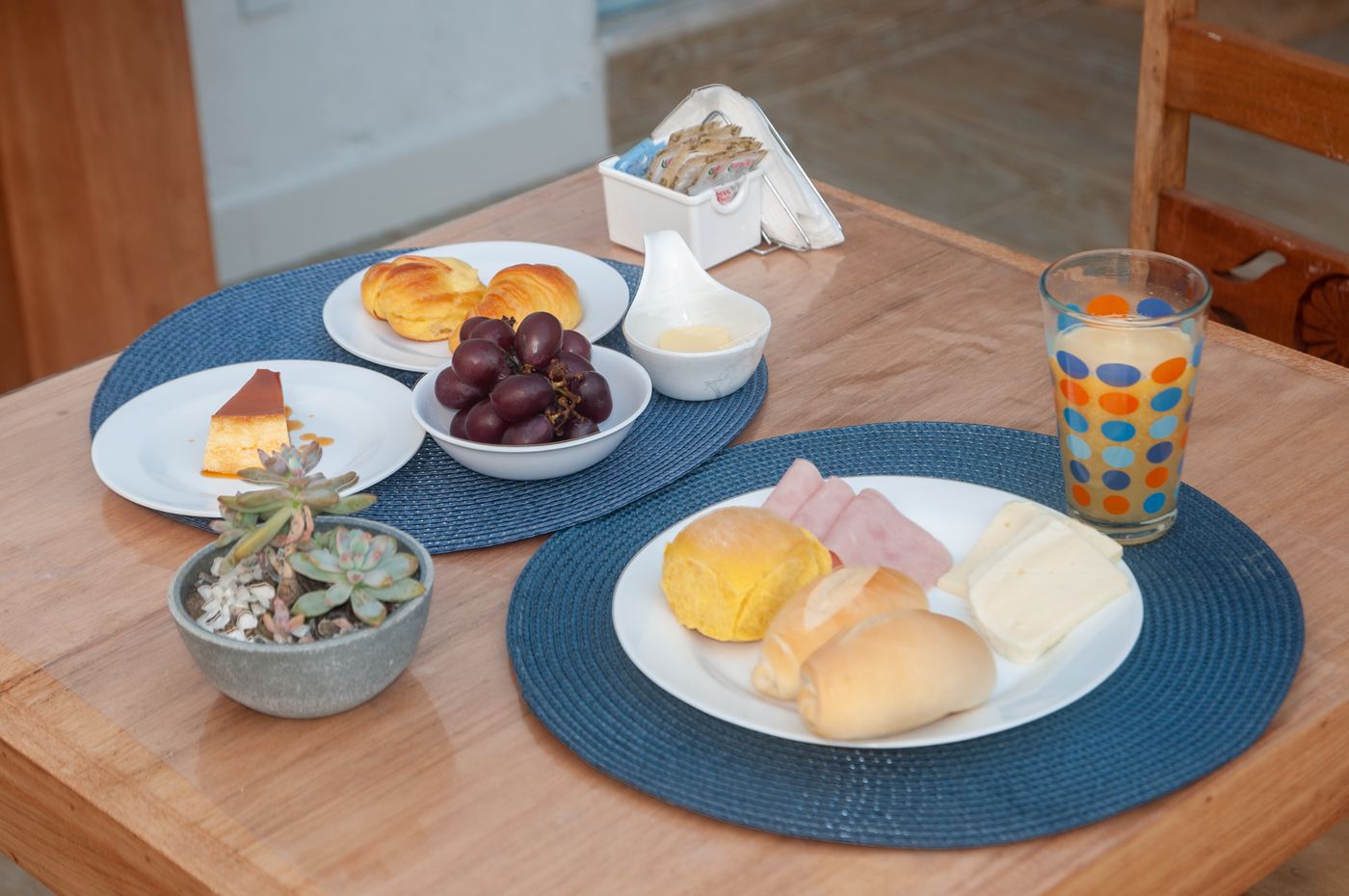 Mesa posta com pães, frios, uvas e pudim
